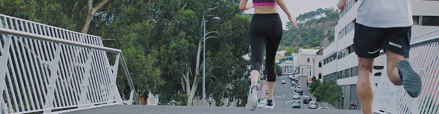 Dos personas corriendo por un puente en medio de una ciudad